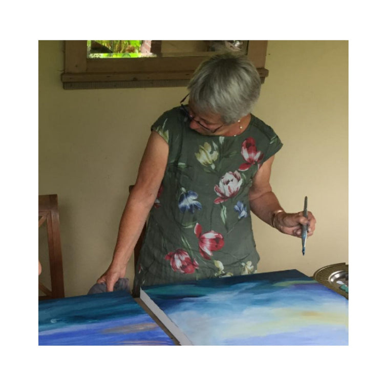 Artist Bettie Huibers looking down at one of her paintings, paint brush in hand