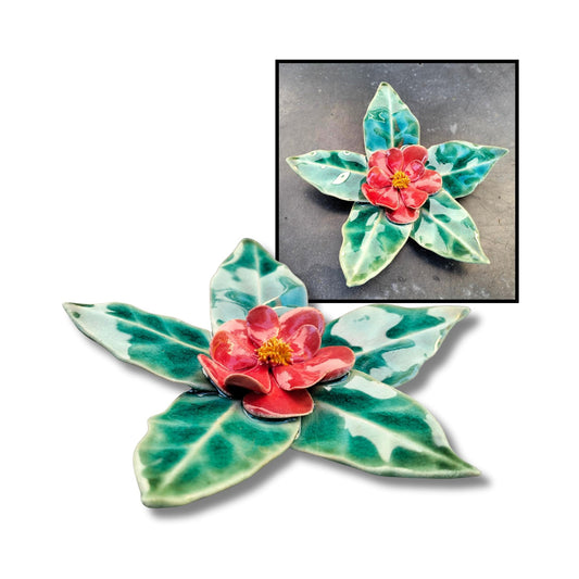 Red camellia flower sculpture with shiny glaze and leaf-shaped base.