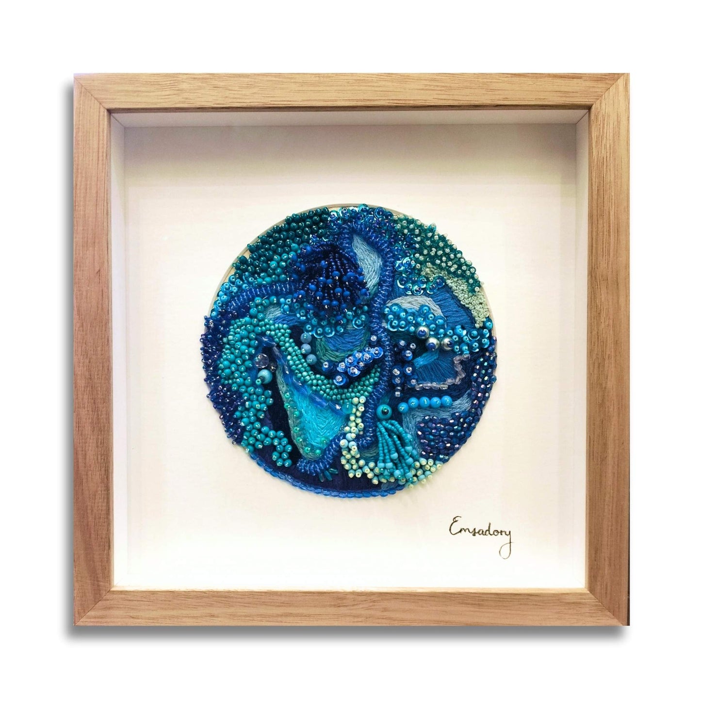 Framed  beaded embroidery artwork with blue and green bead design on a white background, framed in soft brown