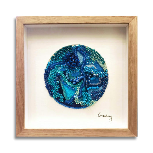 Framed  beaded embroidery artwork with blue and green bead design on a white background, framed in soft brown