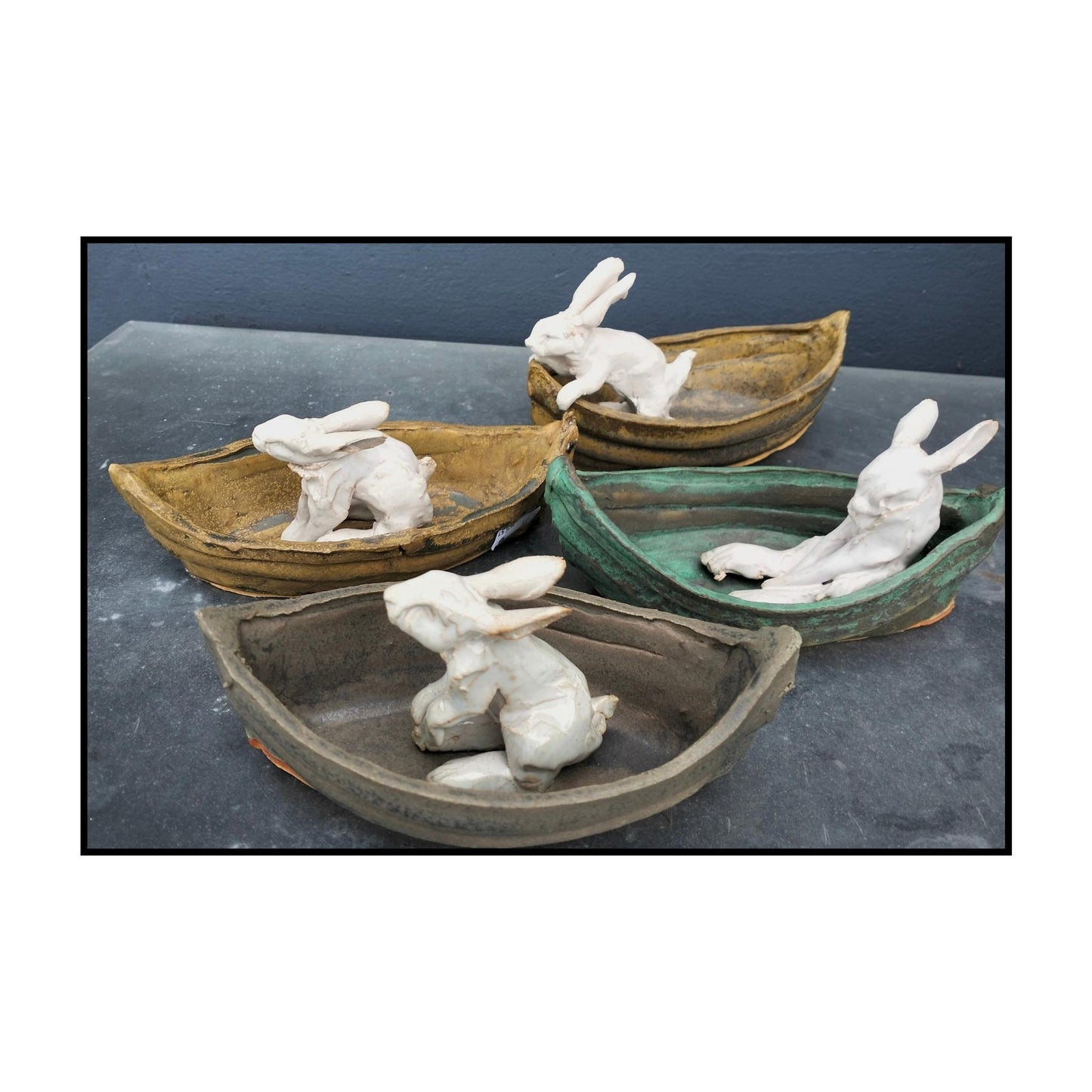 Four ceramic white bunnies in boats all in different poses, by artist Kylie Matheson