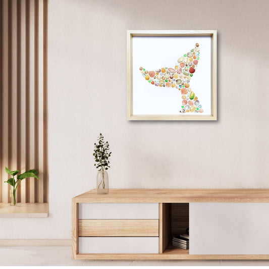 Frolicking Whale sea glass artwork by Steffi Tregenna featuring multicoloured shells, sea glass, and paua in a whale tail shape, framed in pale wood in lifestyle mock up.