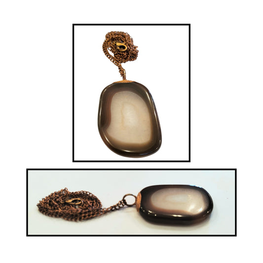 Close-up of natural manganese agate pendant showing earthy brown border and translucent white center with copper setting.