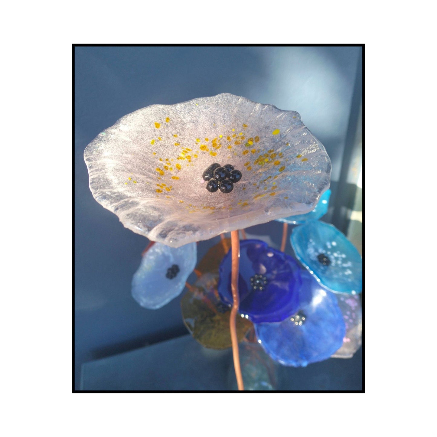 Close-up of a pale clear and yellow dot glass flower with a dark centre and bent copper stem