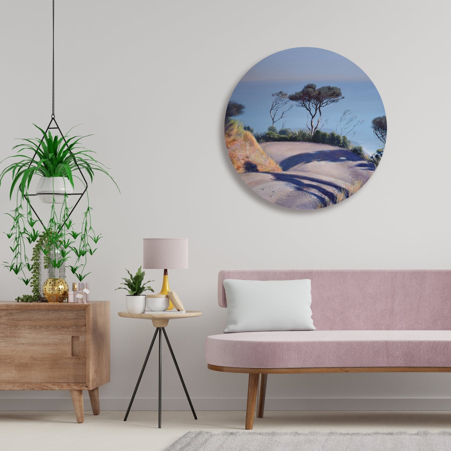 Living room with pink sofa, round wall art of a painting of the road to Anawhata beach and decorative items.