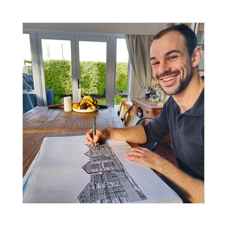 Nathan Kaye seated at a table, focused intently as he works on a detailed fine line pen drawing.