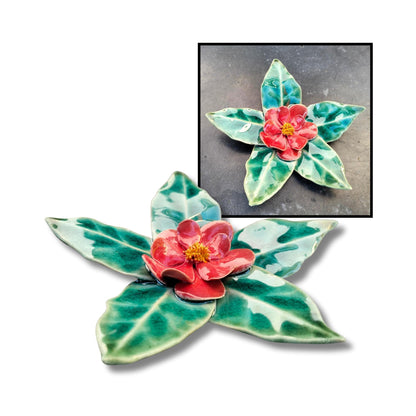 Red camellia flower sculpture with shiny glaze and leaf-shaped base.