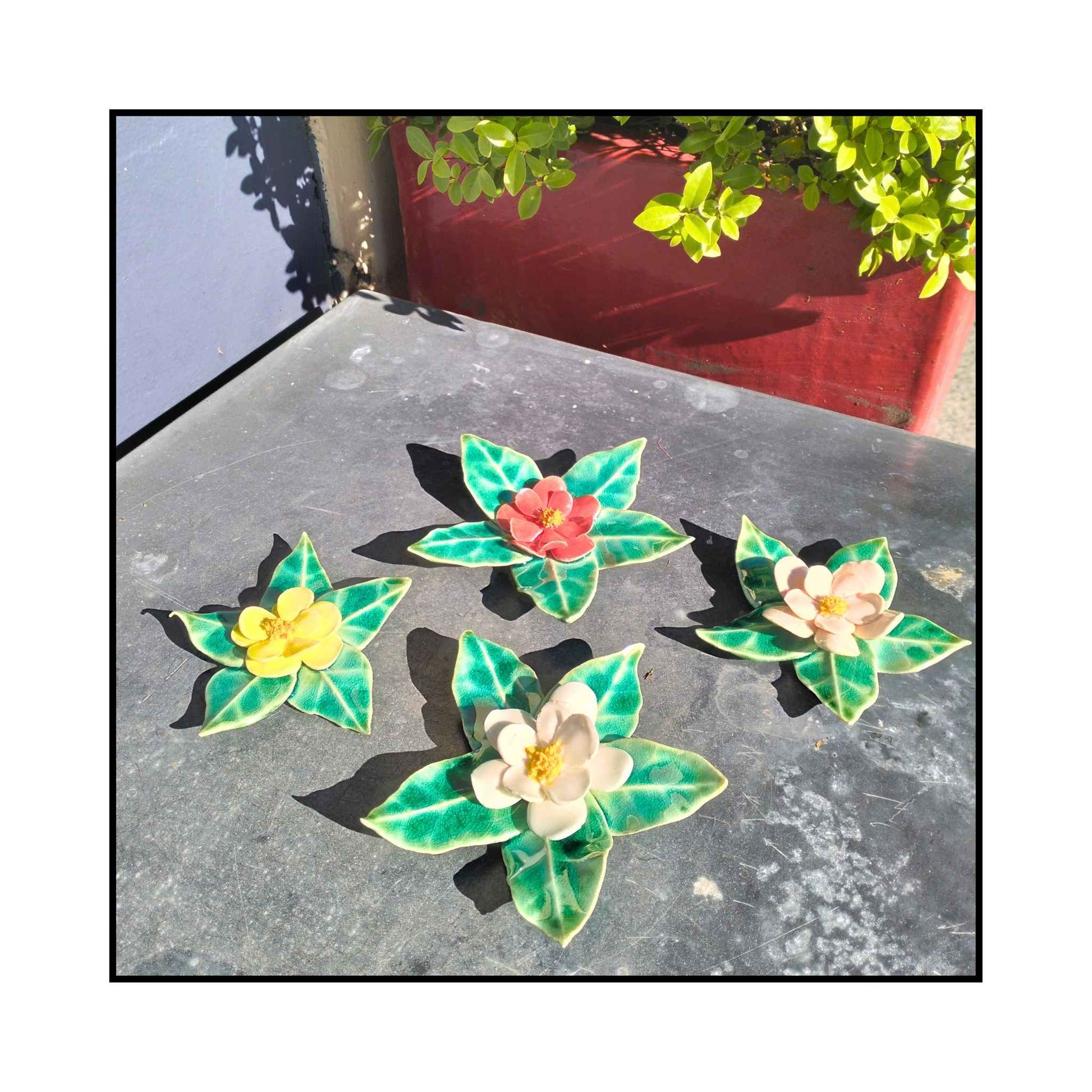 Four handmade ceramic camellia wall flowers in pink, red, white, and yellow with sculpted leaves and glossy glaze.