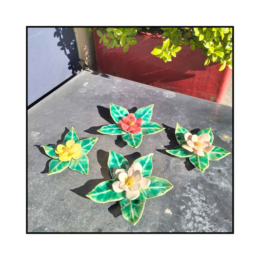 Four handmade ceramic camellia wall flowers in pink, red, white, and yellow with sculpted leaves and glossy glaze.