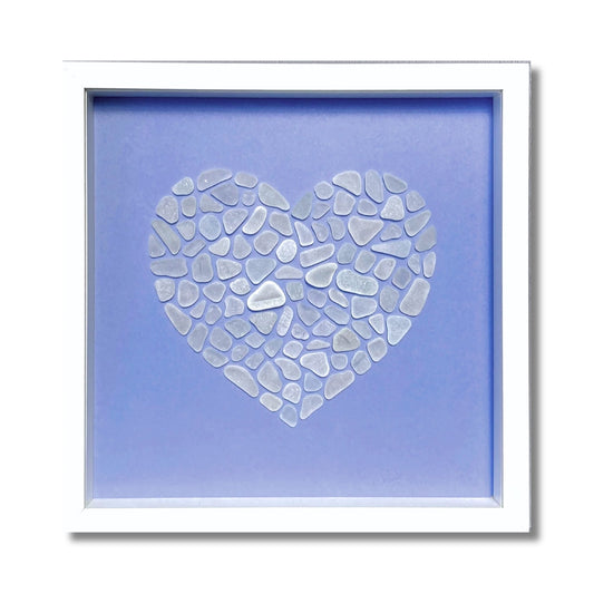 Framed heart shape made from white frosted sea glass pieces arranged on soft blue background in white frame