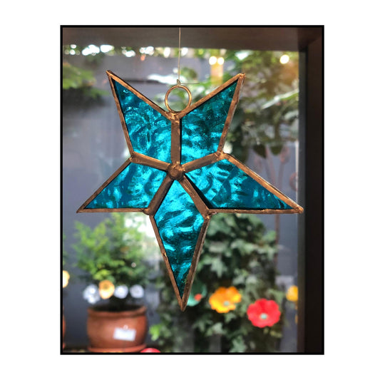 Blue textured glass leadlight star with copper frame by Jenni Foster hanging against blurred background

