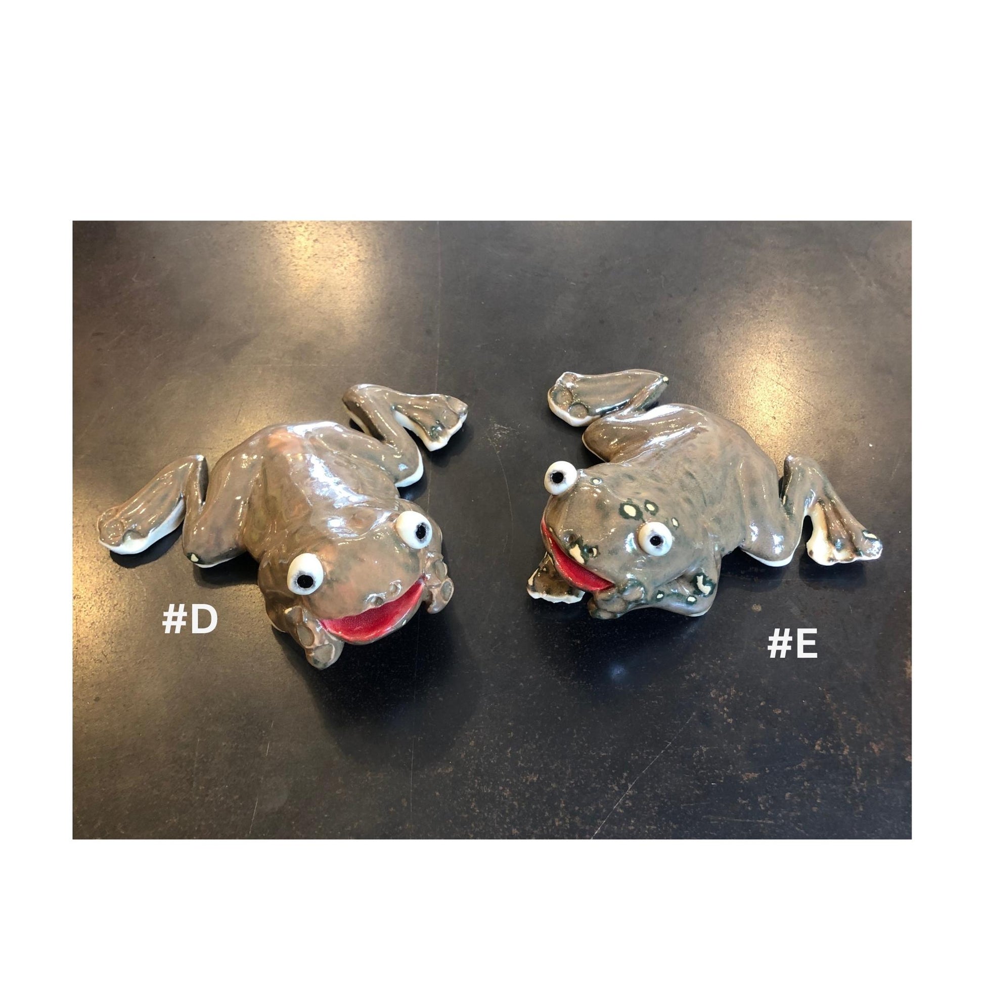 Two handmade brown ceramic frog for the garden, on a dark surface with '#D' and '#E' labels.