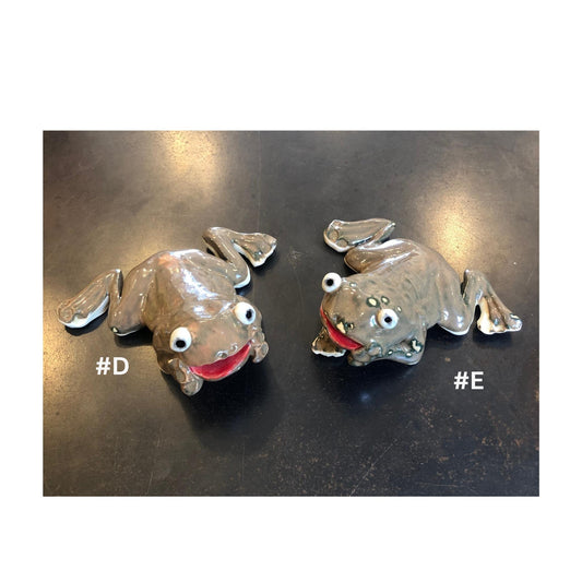 Two handmade brown ceramic frog for the garden, on a dark surface with '#D' and '#E' labels.