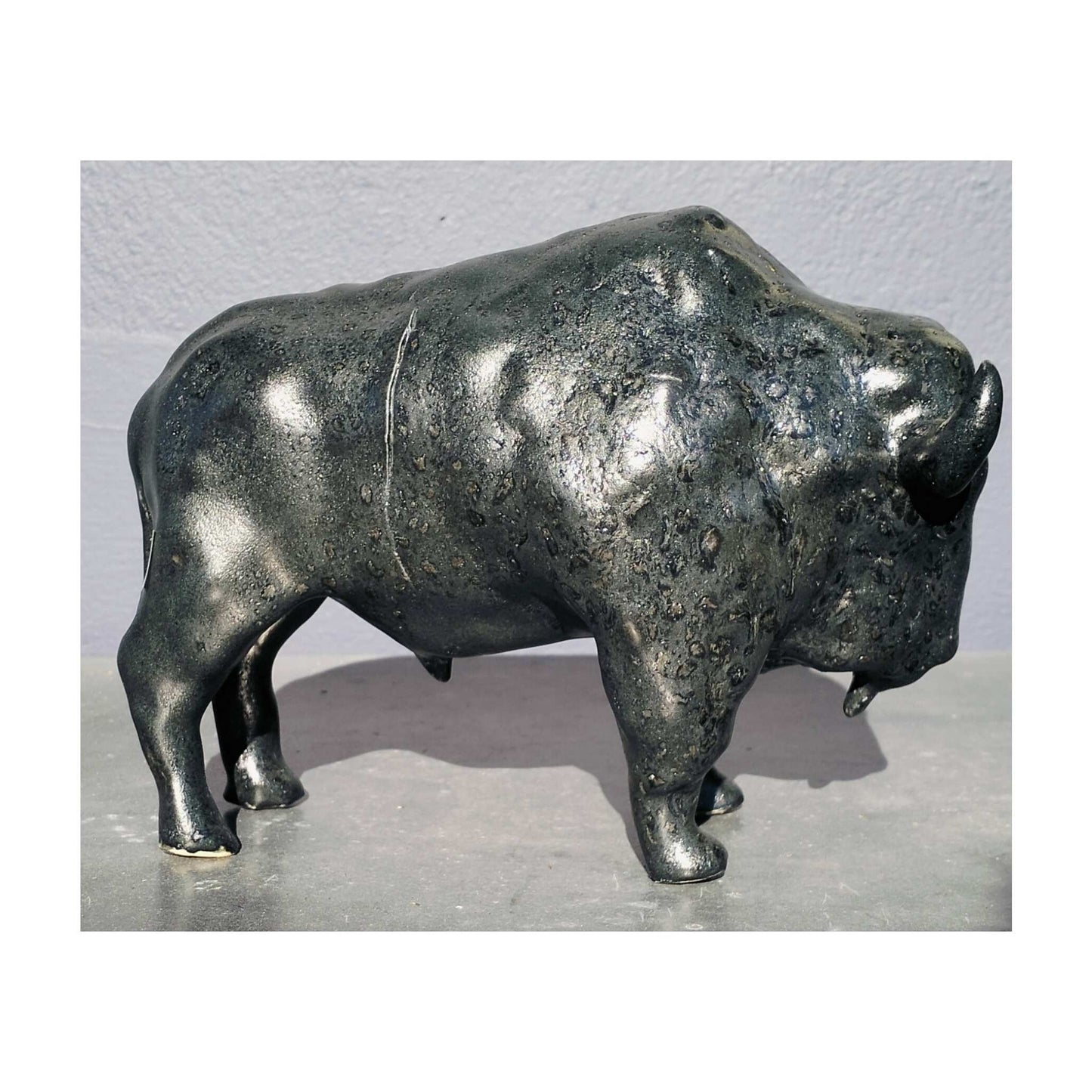 Handmade ceramic buffalo sculpture by Storm Davenport with smooth contours and a black glaze showing green and earthy brown tones.