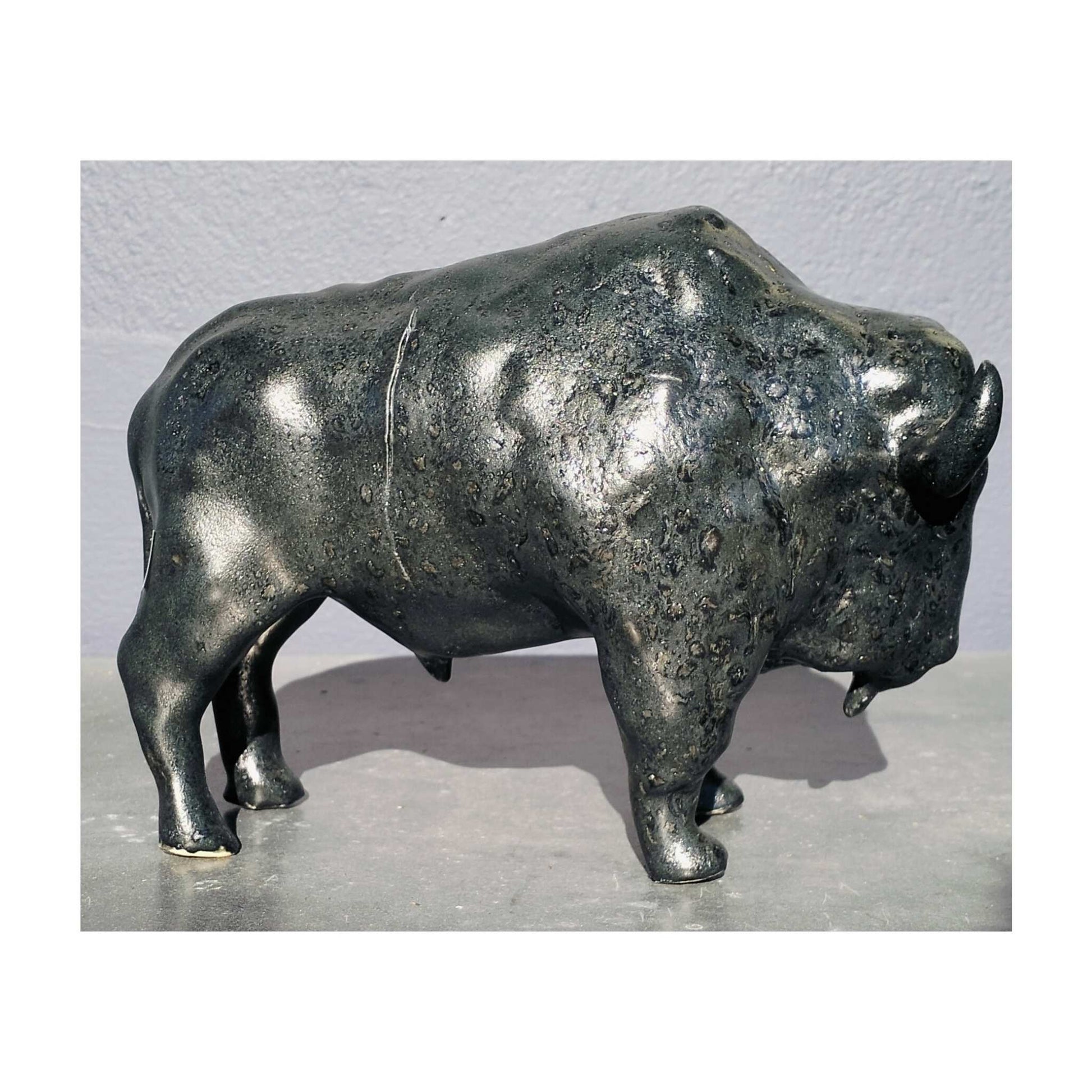 Handmade ceramic buffalo sculpture by Storm Davenport with smooth contours and a black glaze showing green and earthy brown tones.