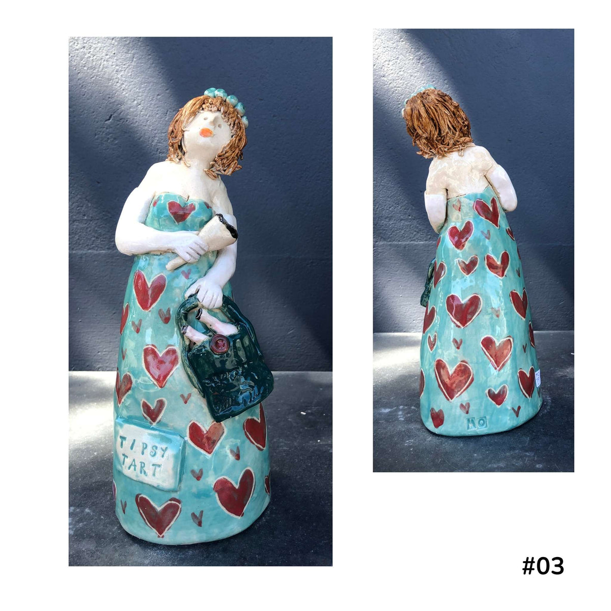 Mandy Olson’s ceramic lady 03, with brown hair, a blue dress with red heart shape pattern, she is holding a wine glass and a bag with two bottles of wine, shown from the front and back.