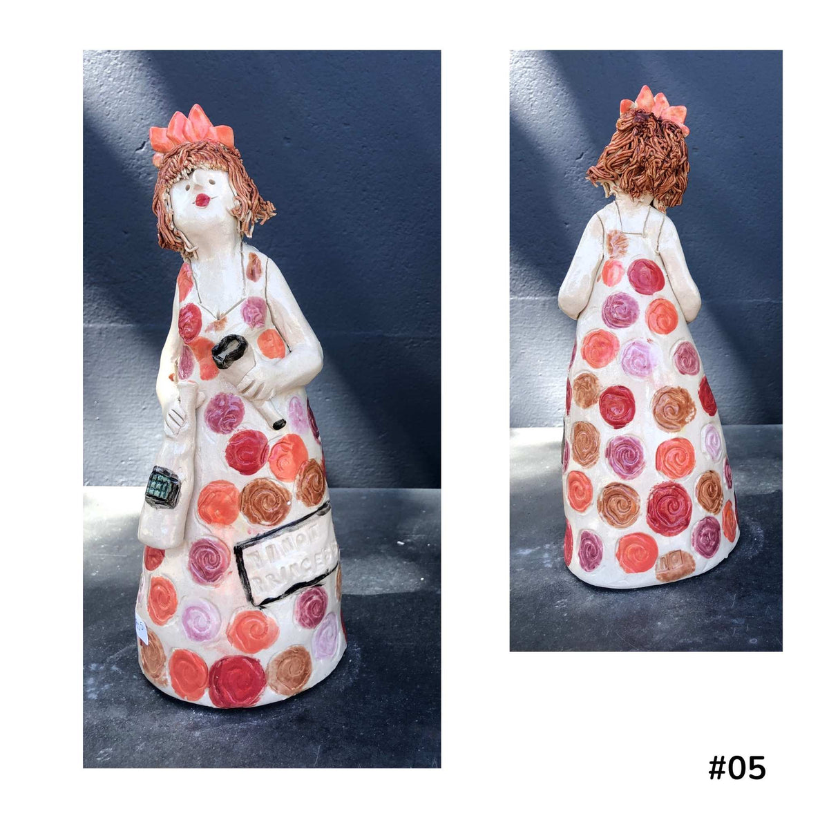 Mandy Olson’s ceramic lady 57, with reddy brown hair, a white dress with colourful koru shape pattern, she is holding a wine glass and a bottle of wine, shown from the front and back.
