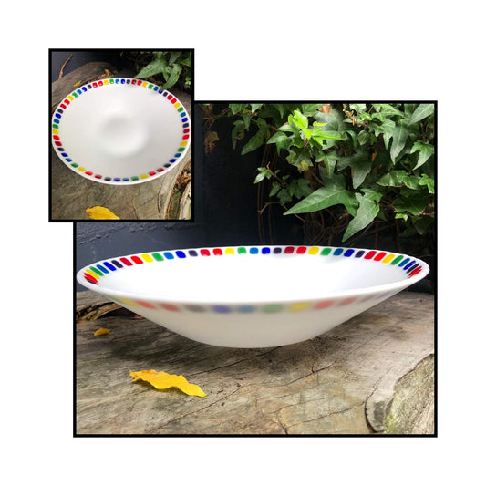 Opaque white fused glass bowl with red, orange, yellow, blue, and purple square accents around the rim, handcrafted by Jill Matthew.