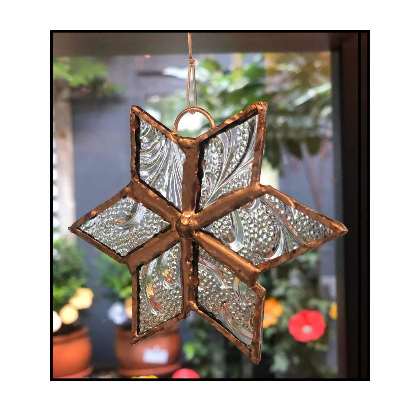 Clear textured glass leadlight star with copper frame by Jenni Foster hanging against blurred background
