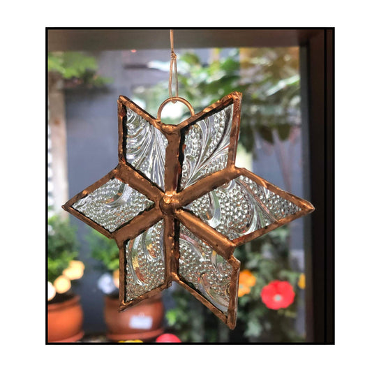 Clear textured glass leadlight star with copper frame by Jenni Foster hanging against blurred background
