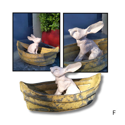 Charming Drifter figure resting with front legs down in a soft brown ceramic boat, handmade by New Zealand artist Kylie Matheson.