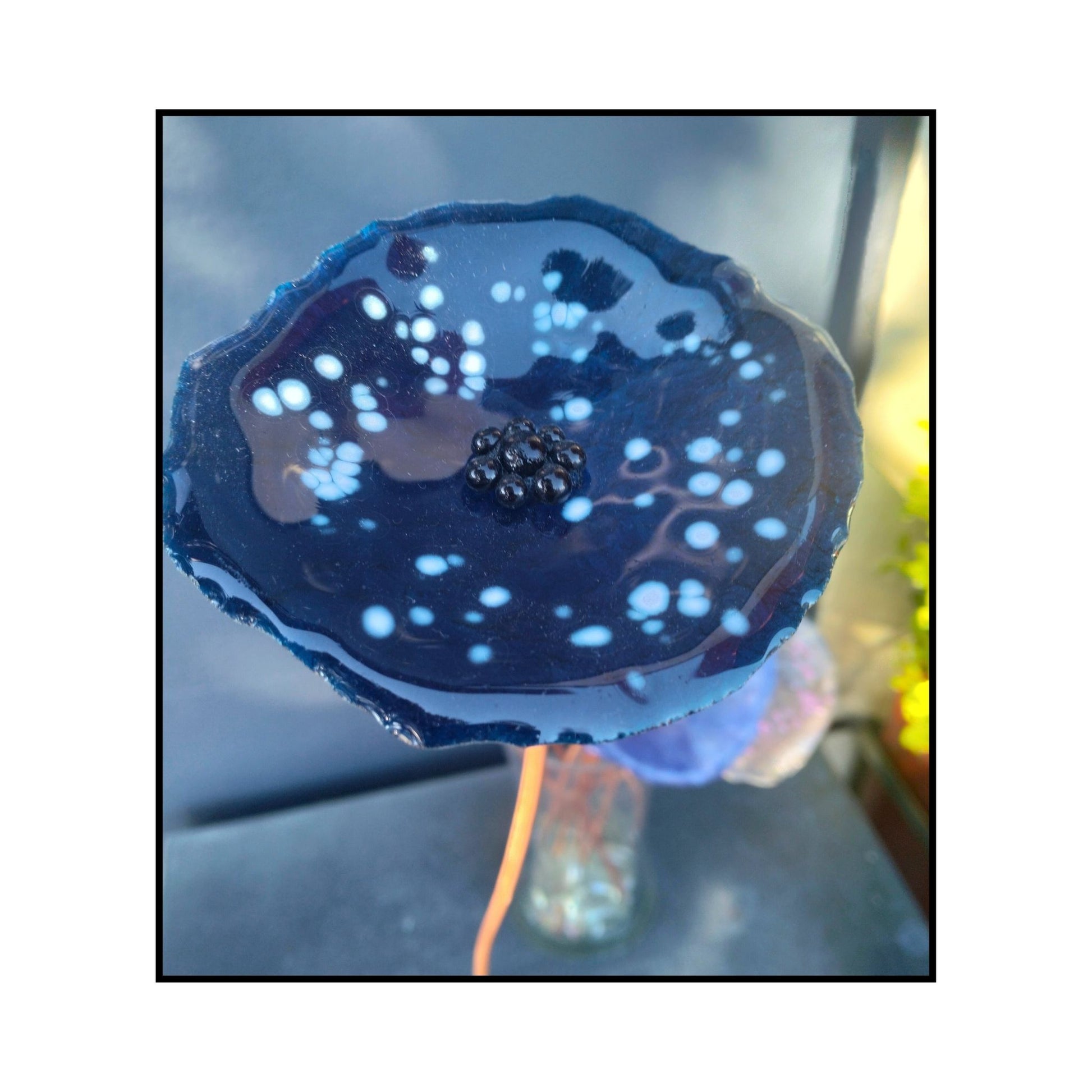 Close-up of a blue with white dots glass flower with a dark centre and bent copper stem