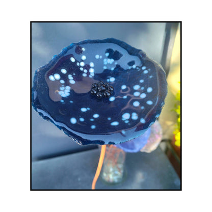 Close-up of a blue with white dots glass flower with a dark centre and bent copper stem