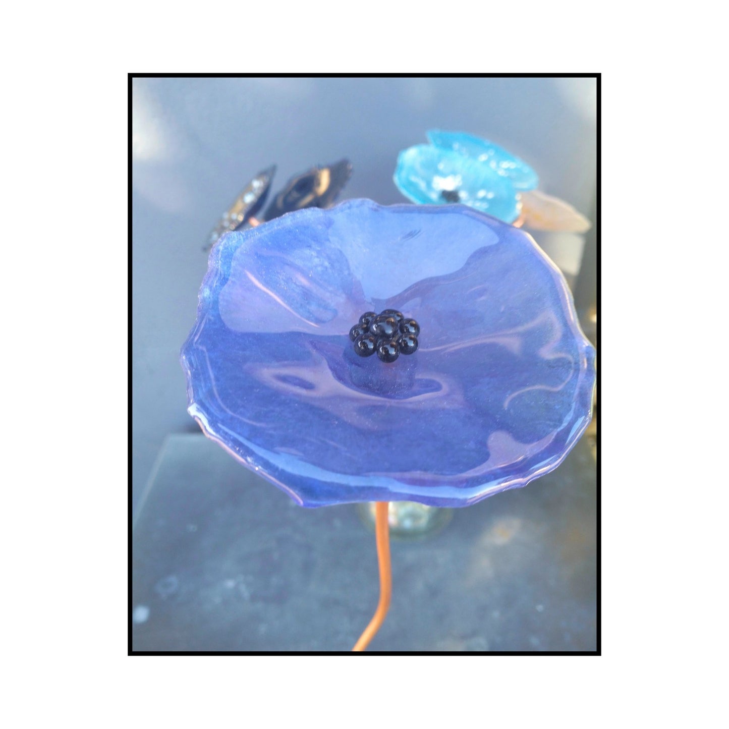 Close-up of a blue glass flower with a dark centre and bent copper stem
