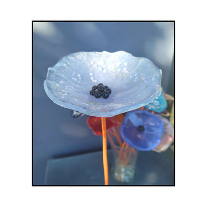 Close-up of a soft pale blue glass flower with a dark centre and bent copper stem