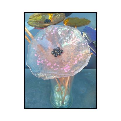 Close-up of a soft pink glass flower with a dark centre and bent copper stem