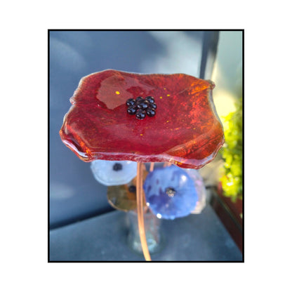 Close-up of a red glass flower with a dark centre and bent copper stem
