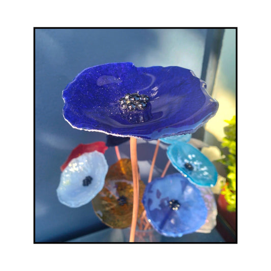 Close-up of a blue glass flower with a dark centre and bent copper stem