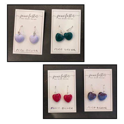 Four pairs of Jenni Foster’s glass heart earrings in pale mauve, deep green, red and purple, with handmade sterling silver earwires on display cards.
