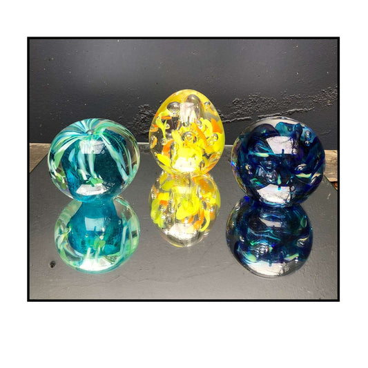 Three colorful glass paperweights on a reflective surface with a dark background