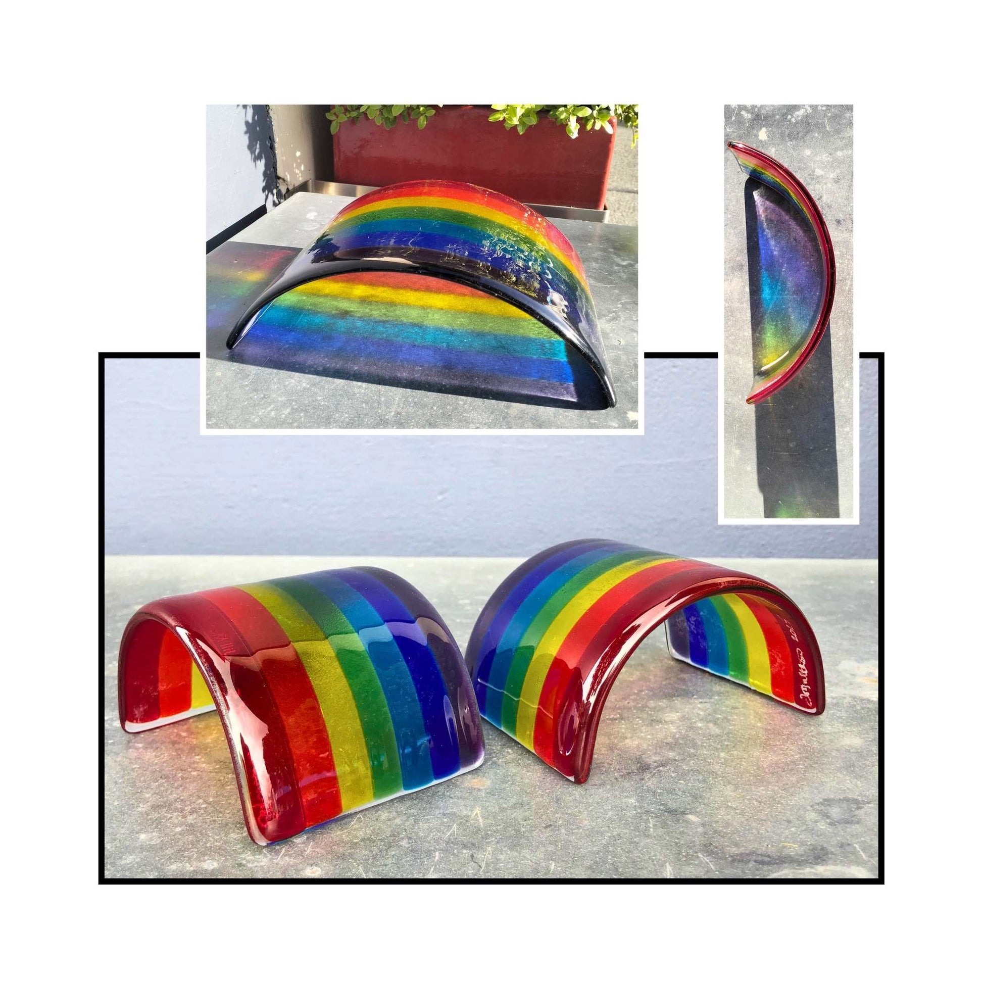 Medium fused glass rainbow with reflection sitting on a metal surface with bush behind.