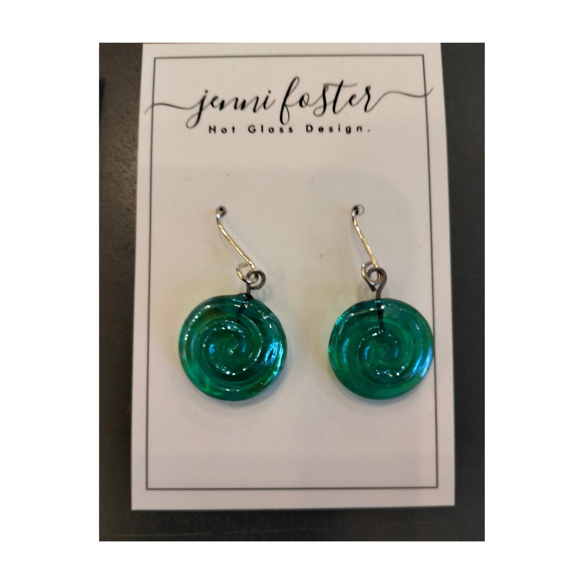 Jenni Foster’s round glass koru earrings in green,  displayed on jewellery card.