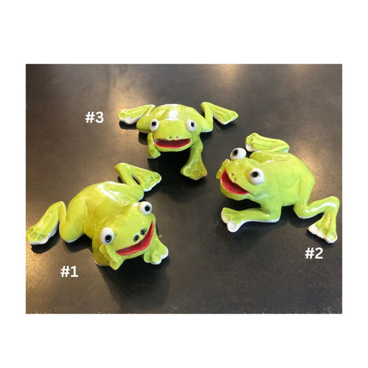 Three lime green ceramci frog figurines on a reflective surface with numbers indicating their order.