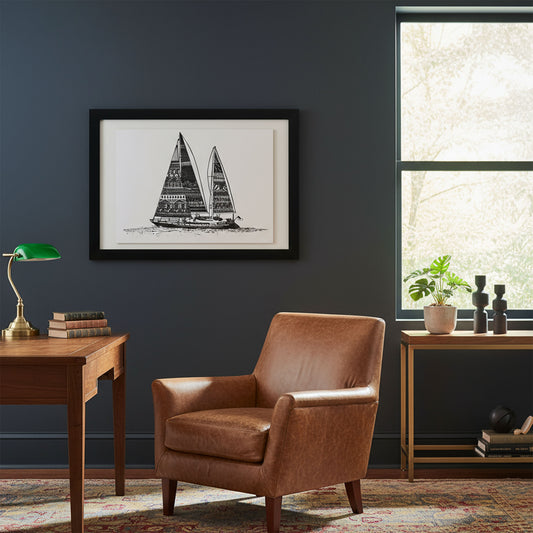 Brown leather armchair in a room with a framed sailboat print on the wall, a desk, and a window.