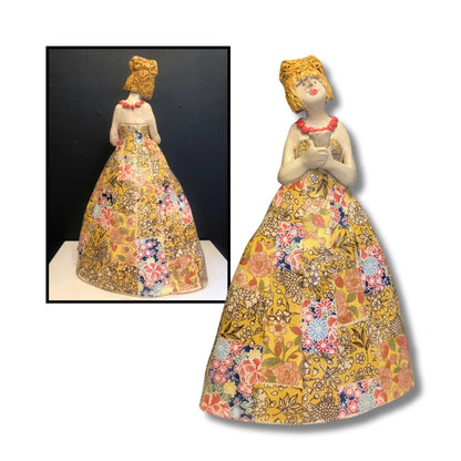 Hand-painted ceramic sculpture of woman in yellow floral patchwork gown with coral necklace on white background