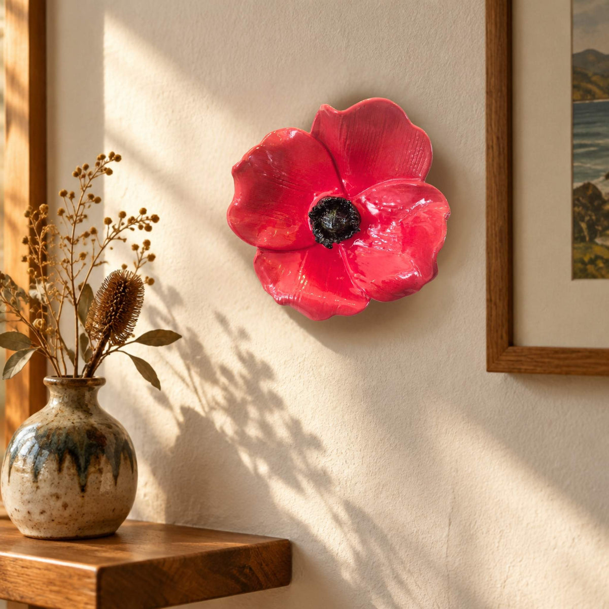 Red Ceramic wall Poppy by artist Teresa Corbishley hanging on awall with a vase and a picture
