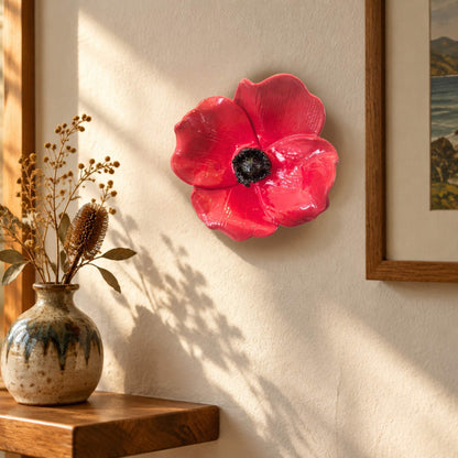 Red Ceramic wall Poppy by artist Teresa Corbishley hanging on awall with a vase and a picture
