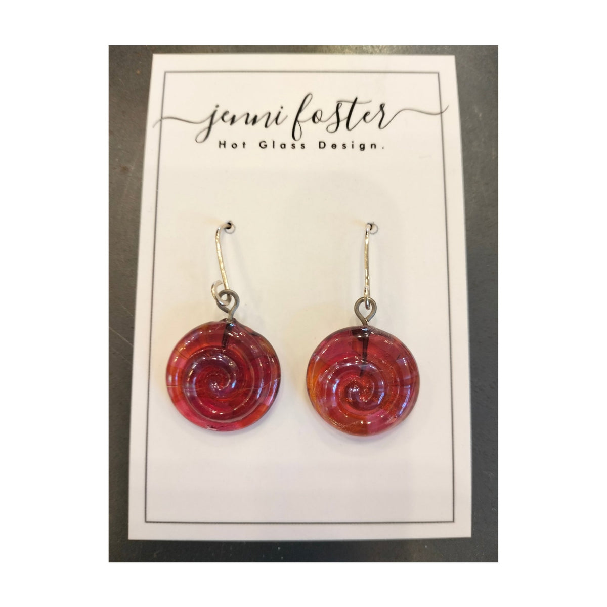 Jenni Foster’s round glass koru earrings in red,  displayed on jewellery card.
