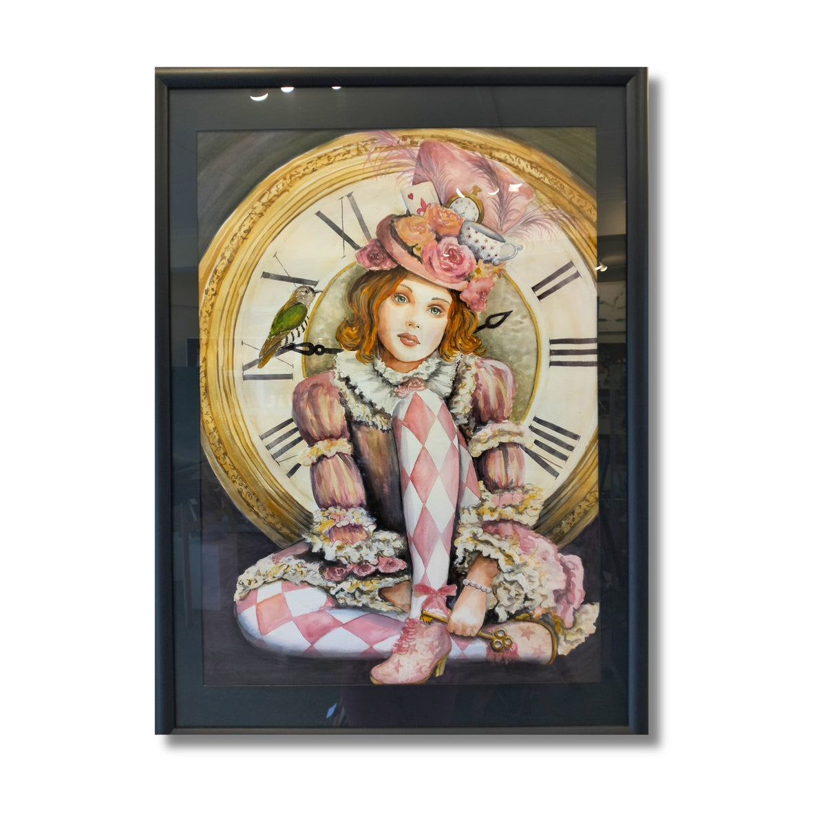 A framed art print featuring a whimsical illustration of Alice in Wonderland in a pink and white harlequin dress and hat, seated in front of a large clock face, enclosed in a black frame.