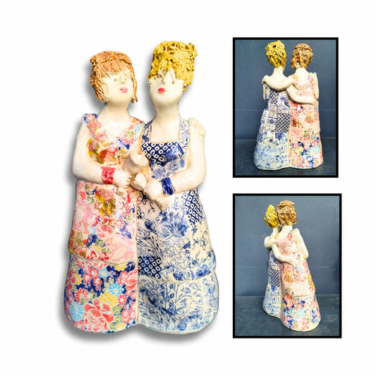 Two handmade ceramic sister figurines with wine glasses, colourful dresses, and quirky expressions – by New Zealand artist Mandy Olson.

