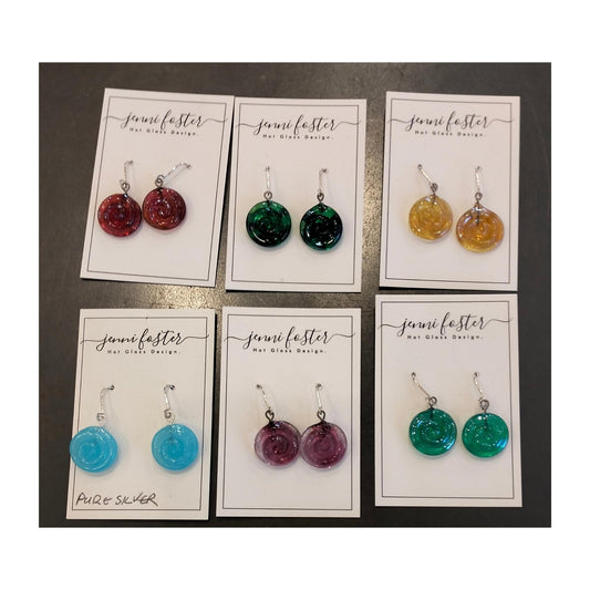 Six pairs of Jenni Foster’s round glass koru earrings in red, dark green, amber, light blue, purple and turquoise, displayed on jewellery cards.
