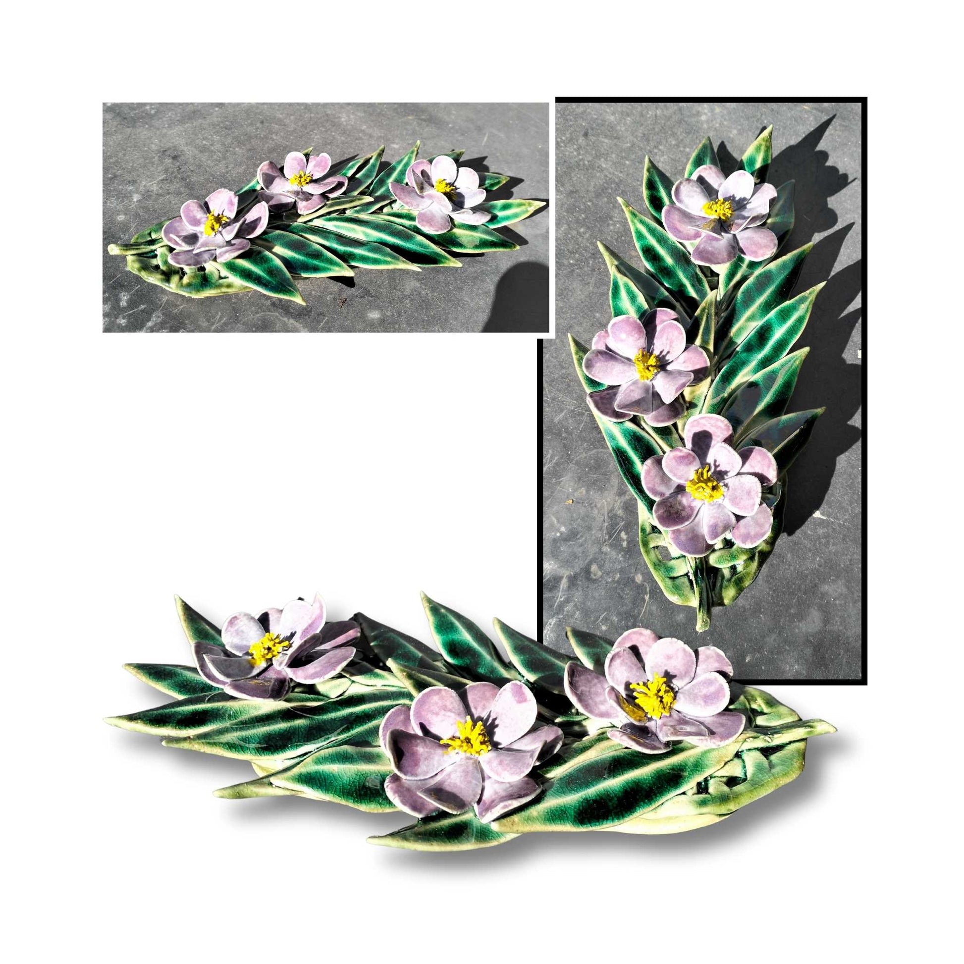 Deep purple ceramic camellia wall art with three flowers and sculpted foliage.