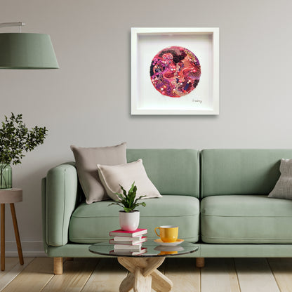 Living room with a green sofa, colorful pink, reds, purple beaded embroidery abstract artwork on the wall, and small table with items.